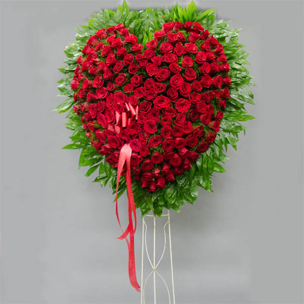 Heart-shaped red rose standing spray with a pink ribbon