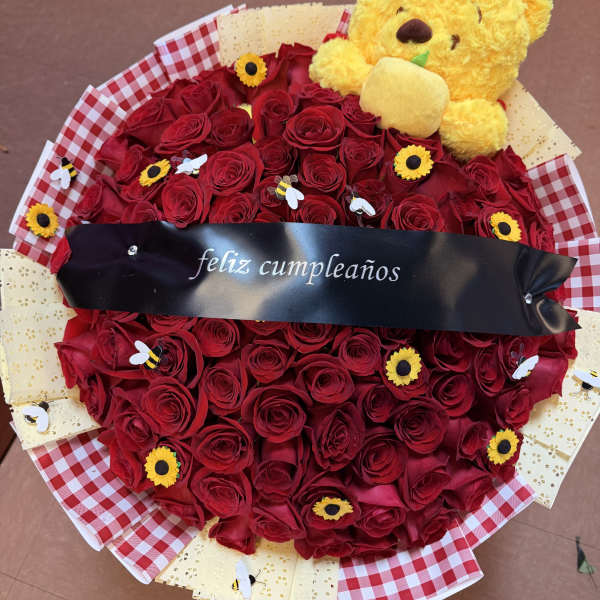 Heart-shaped bouquet of red roses with a yellow teddy bear and birthday ribbon