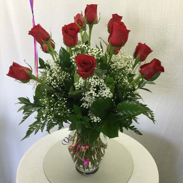 Red roses arranged in a clear glass vase with white filler flowers