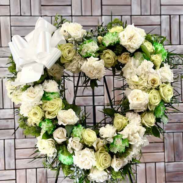 Heart-shaped floral wreath of white and pale green roses on a stand