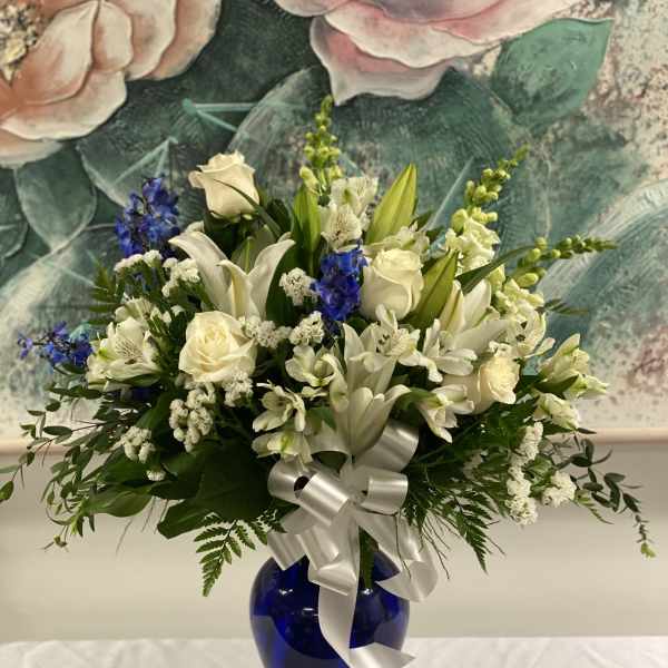 White lilies and roses arranged in a blue vase with a silver ribbon.