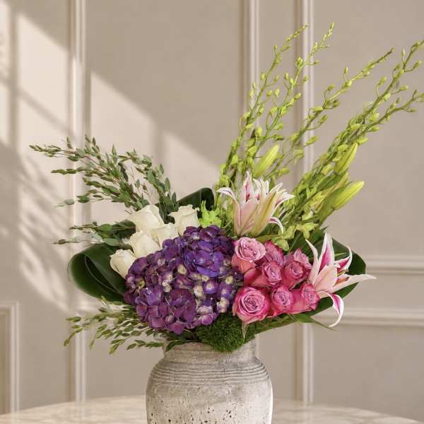 Mixed bouquet with purple hydrangea, pink roses, white lilies, and a ceramic vase