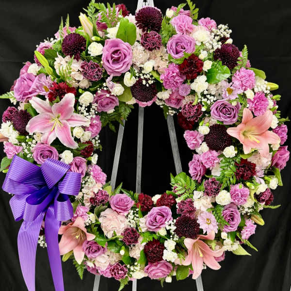 Large pink and purple floral wreath with a ribbon bow on a stand