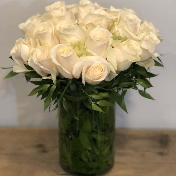 Cream roses arranged in a glass vase with dark green foliage