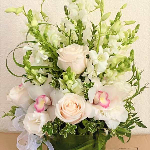 White and pale pink floral arrangement in a green vase with a ribbon