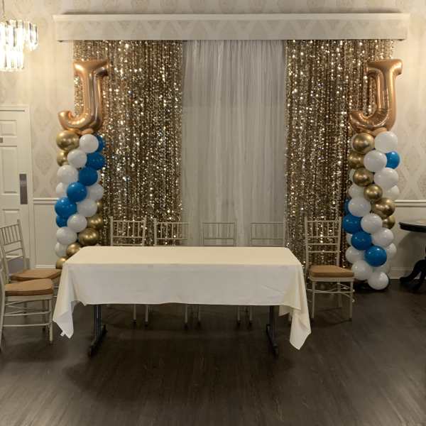 Event backdrop with gold sequin curtains, balloon columns, and a table
