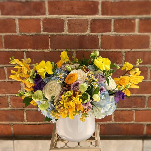 Mixed bouquet of yellow, white, blue, and purple flowers in a white vase