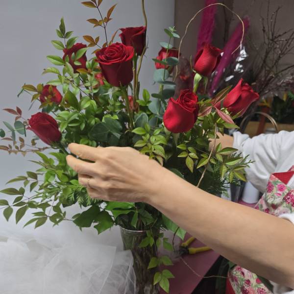 Red roses arranged in a clear glass vase with greenery