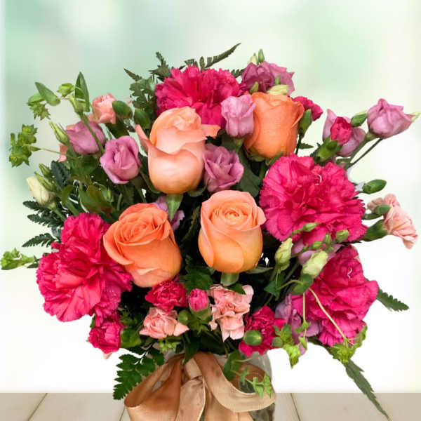Bouquet of orange roses and pink carnations in a glass vase with ribbon