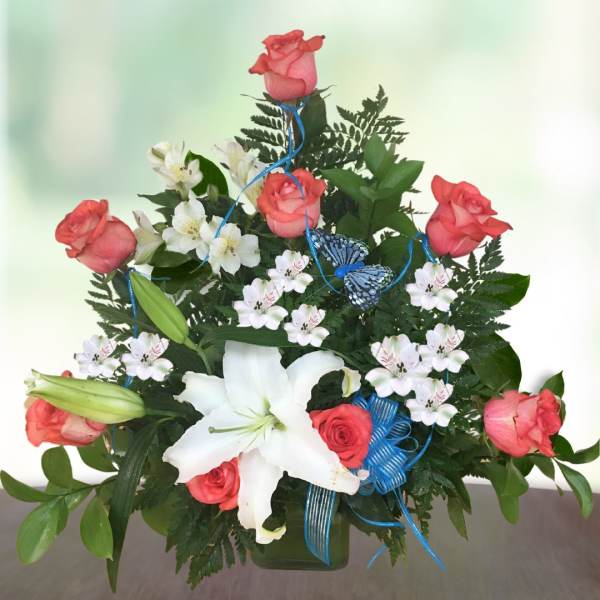 Pink roses and white lilies arranged in a green vase with blue ribbon and butterfly accents.