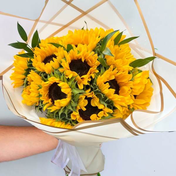 Bouquet of bright yellow sunflowers wrapped in white paper with gold trim