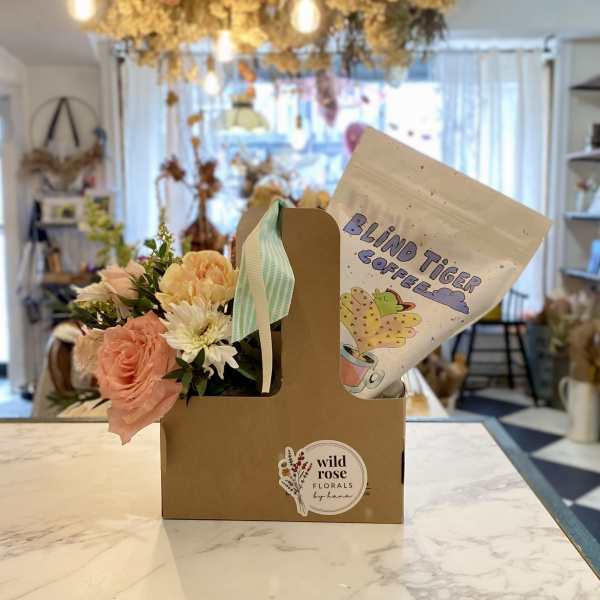 Peach and white bouquet in a cardboard carrier beside a coffee bag