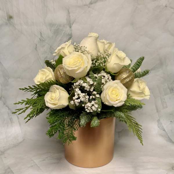 White roses arranged in a gold cylindrical vase with evergreen accents