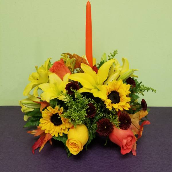 Yellow lilies and sunflowers arranged around a tall orange candle