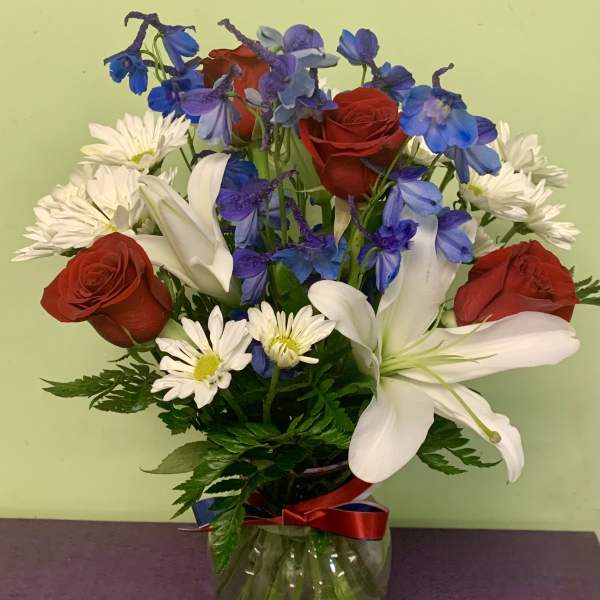 Bouquet of red roses, white lilies, blue flowers, and white daisies in a glass vase