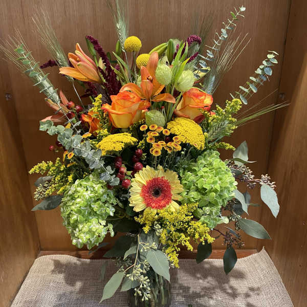 Tall mixed bouquet in a glass vase with orange roses and lilies