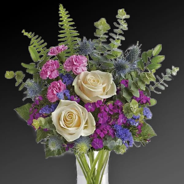 Bouquet of cream roses, pink carnations, and purple filler in a clear vase