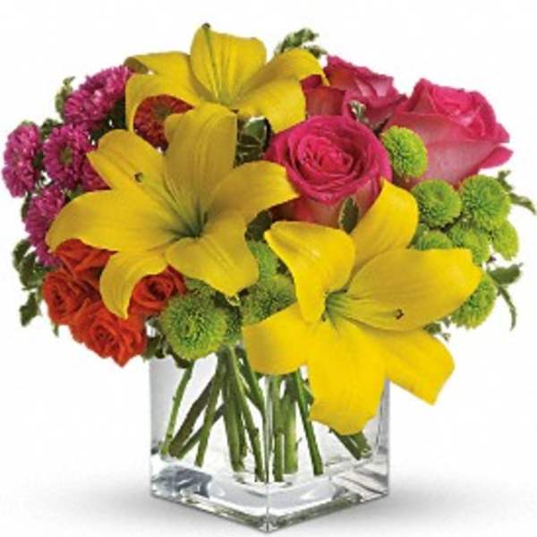 Bouquet of yellow lilies, pink roses, and green pompons in a clear glass vase