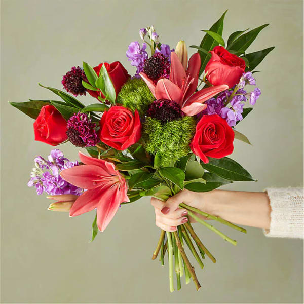 Handheld bouquet of red roses, pink lilies, and purple flowers