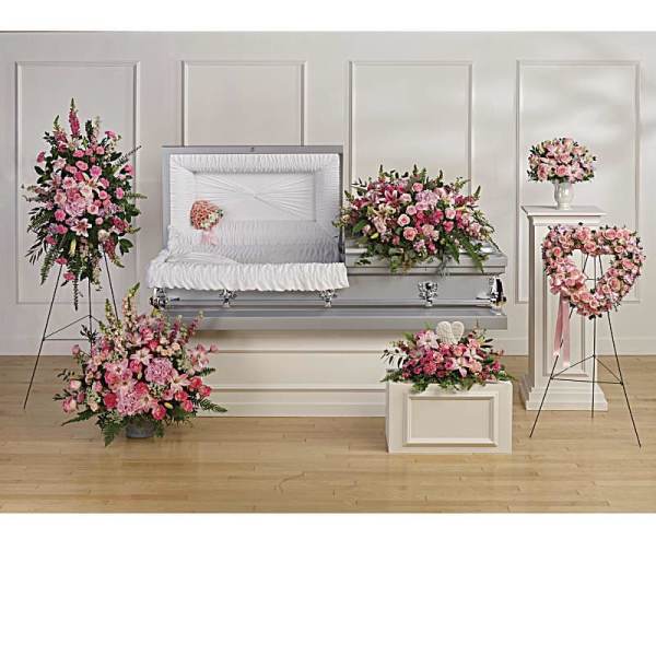 Funeral set with pink floral sprays, casket spray, wreath, and bouquet around an open silver casket.