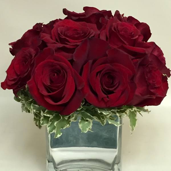 Red roses arranged in a clear glass vase with variegated greenery