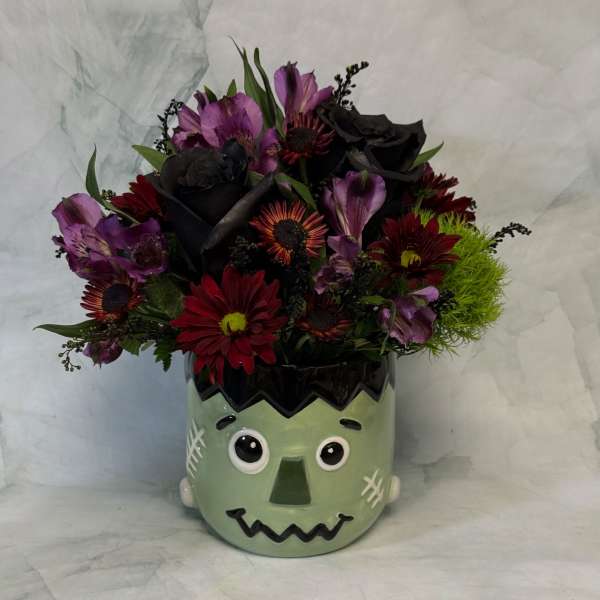 Bouquet of red, purple, and black flowers in a Frankenstein face vase