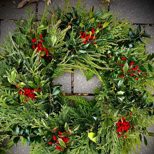 Evergreen wreath with glossy foliage and clusters of bright red berries on a stone surface