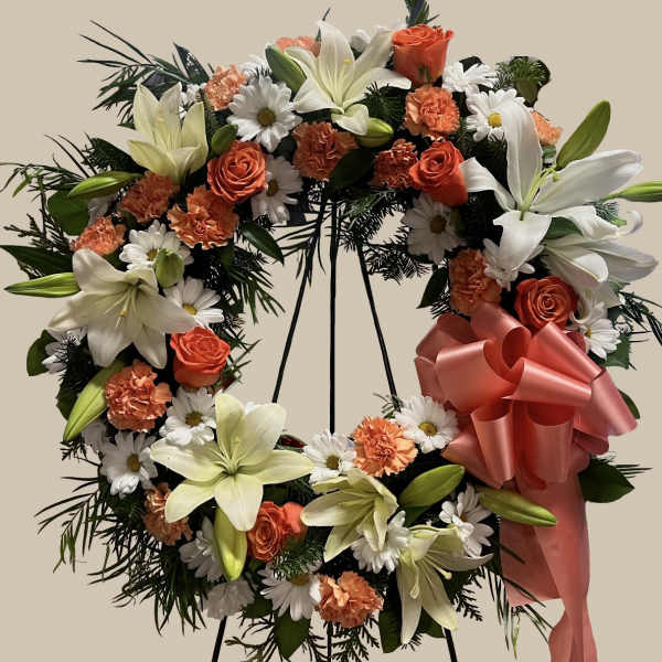 Heart-shaped floral wreath with lilies, roses, daisies, and a pink ribbon bow