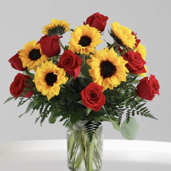 Red roses and yellow sunflowers in a clear glass vase