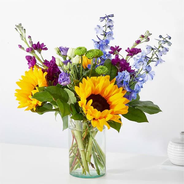 Bouquet of sunflowers, purple blooms, and blue flowers in a clear glass vase