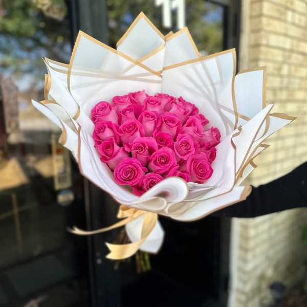 Bouquet of bright pink roses wrapped in white paper with gold trim