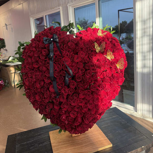 Large heart-shaped arrangement of red roses with a black ribbon and gold butterfly accents