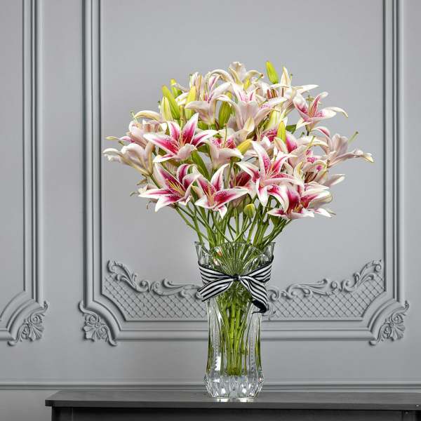 Pink and white lilies in a clear glass vase with a striped ribbon
