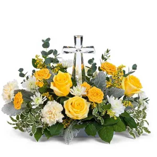 Yellow roses and white flowers arranged around a clear glass cross