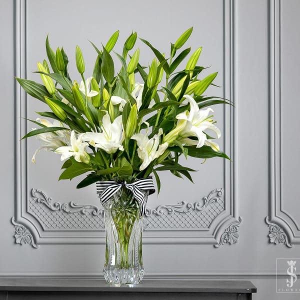 White lilies in a clear glass vase with a striped ribbon