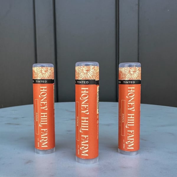 Three orange Honey Hill Farm lip balm tubes standing on a round light blue surface