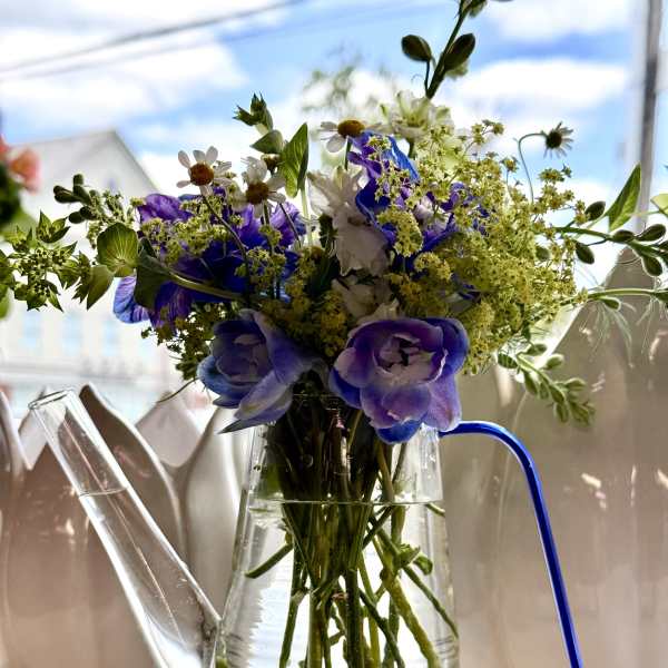 Purple and white flowers arranged in a clear glass watering can vase