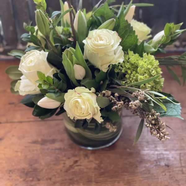 White roses and lilies in a low glass vase with greenery