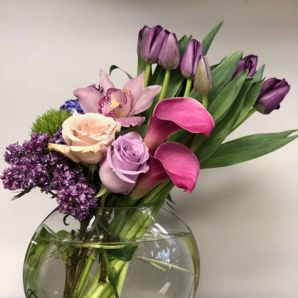 Bouquet of purple tulips, pink calla lilies, roses, and orchids in a glass vase