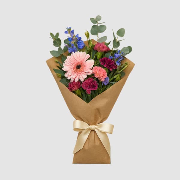 Bouquet of pink, blue, and magenta flowers wrapped in brown paper with a ribbon