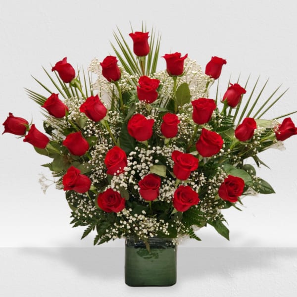 Large fan-shaped arrangement of red roses and white filler flowers in a green glass cube vase