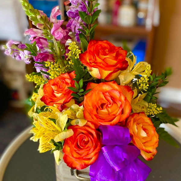 Bouquet of orange roses and purple flowers in a wooden container with a purple ribbon