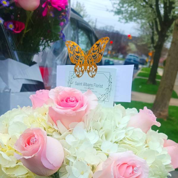 Pink roses in a white box with pale hydrangeas and a butterfly card topper