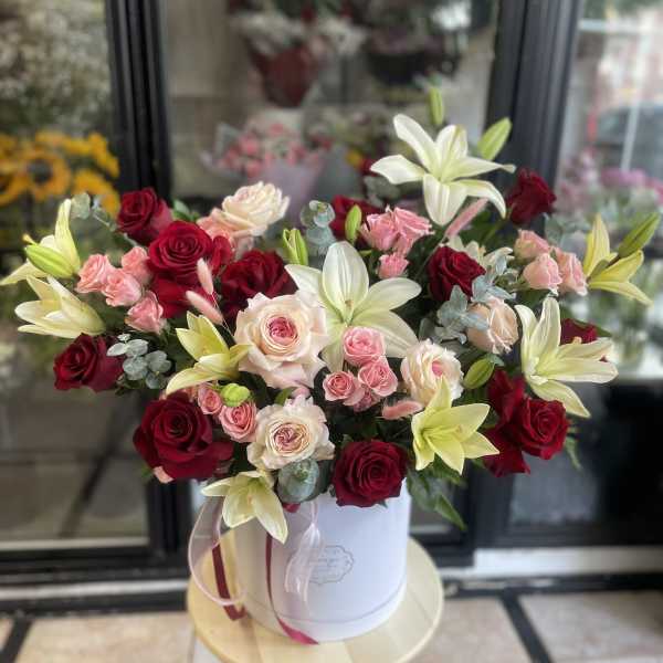Bouquet of red and blush roses with white lilies in a white hat box