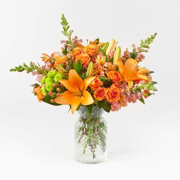 Orange lilies and roses arranged in a clear glass vase