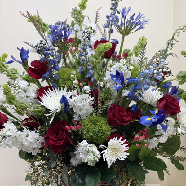 Basket arrangement of red roses, white daisies, and blue flowers