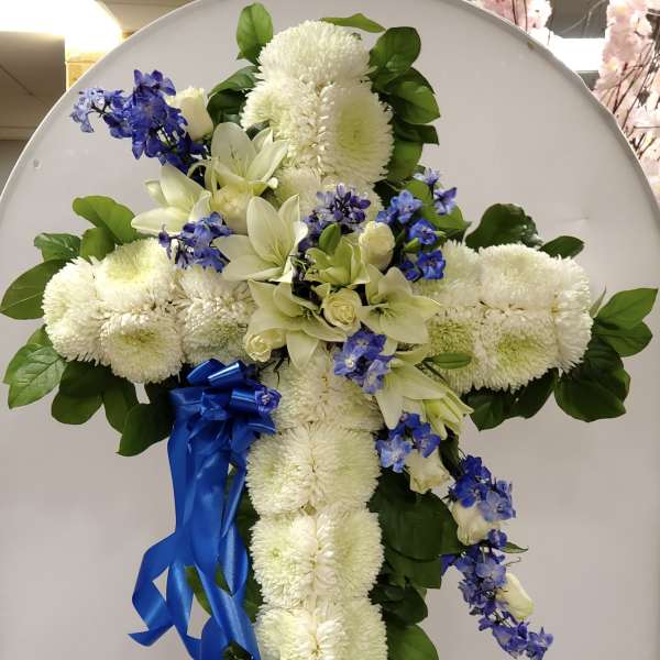 White floral cross arrangement with blue ribbon on an easel
