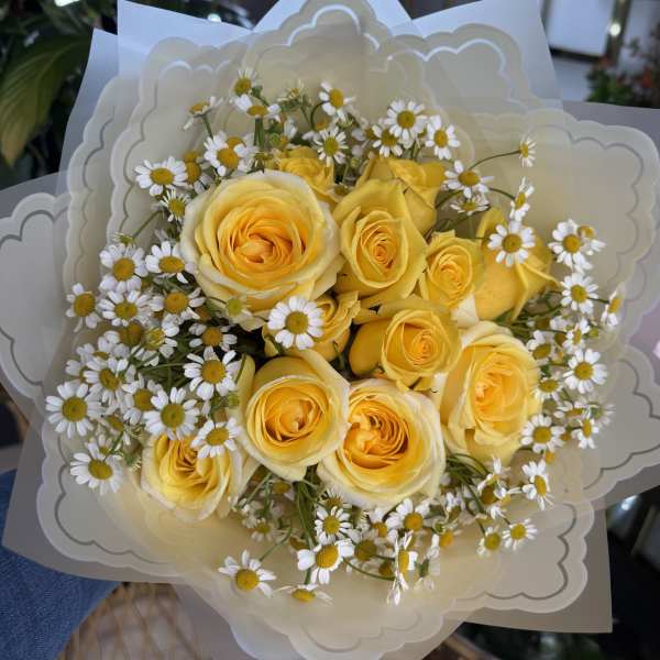 Bouquet of yellow roses and small white daisies wrapped in cream paper