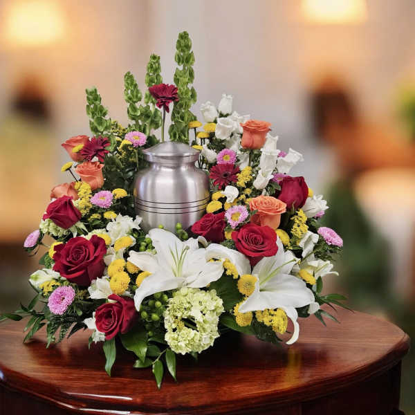 Floral funeral urn arrangement with roses and lilies around a silver urn