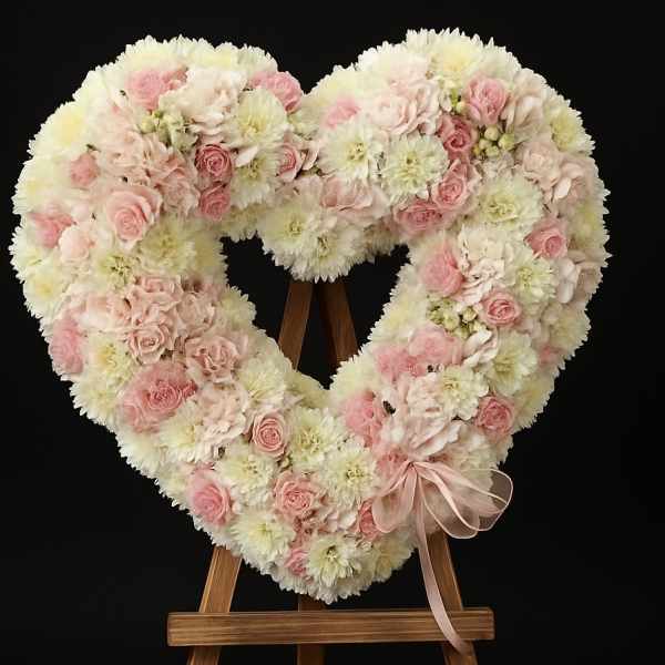 Heart-shaped wreath of white and pale pink flowers on a wooden easel